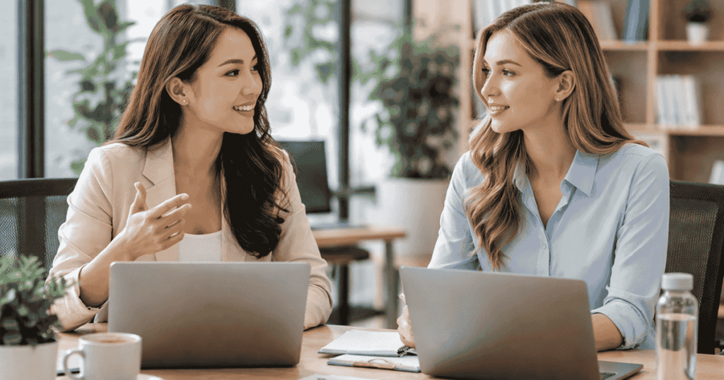 two young female employees talking and discussing office and laptops on table - NDA for startups